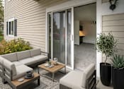 Thumbnail 4 of 11 - A patio with a grey couch, a wooden coffee table, and a potted plant.
