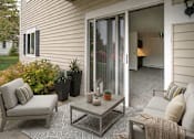 Thumbnail 10 of 11 - A patio with a grey couch, a grey chair, a grey coffee table and a grey rug.