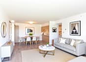 Thumbnail 8 of 13 - A living room with a grey couch, a white coffee table, a dining table with chairs, and a mirror on the wall.
