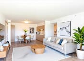 Thumbnail 2 of 13 - A living room with a white couch, a coffee table, and a dining table with chairs.