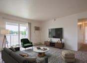 Thumbnail 8 of 11 - A living room with a grey couch, a green chair, a coffee table, and a television.