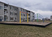 Thumbnail 31 of 33 - A playground with a swing set in front of apartment buildings.