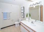 Thumbnail 11 of 13 - A white toilet sits in a bathroom next to a sink and a mirror.