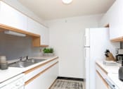 Thumbnail 9 of 10 - A small kitchen with white cabinets and a white fridge.
