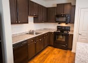 Thumbnail 25 of 32 - A kitchen with dark wood cabinets and a black stove top oven.