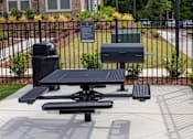 Thumbnail 15 of 25 - A black picnic table with a trash can and a recycling bin in front of a black fence.