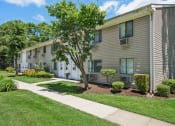 Thumbnail 4 of 37 - Outside view of apartment with a sidewalk and trees in front at Brookwood at Ridge, New York, 11961