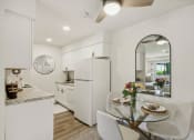 Thumbnail 5 of 37 - a white kitchen with granite counter top and dining area with a glass table and chairs at Brookwood at Ridge, New York, 11961