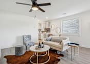 Thumbnail 7 of 48 - A living room with a white couch, a grey armchair, a round table with a bottle on it, and a brown cowhide rug.
