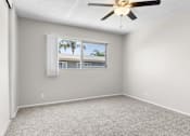 Thumbnail 11 of 17 - A room with a ceiling fan and a window with a view of a building and palm trees.