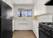 Thumbnail 8 of 17 - A black refrigerator sits in a kitchen with white cabinets and a black stove.