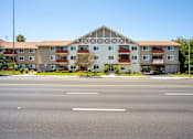 Thumbnail 69 of 69 - A large building with a white and brown facade sits next to a road.