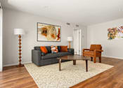 Thumbnail 11 of 69 - A living room with a grey couch, a brown chair, and a painting on the wall.