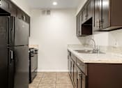 Thumbnail 3 of 36 - A kitchen with a black refrigerator and brown cabinets.
