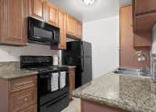 Thumbnail 13 of 41 - Studio apartments in Mar Vista CA - Vista - Kitchen with Sandy Granite Countertops, Wooden Cabinetry, Microwave, Oven, Stove, and Refrigerator, and Dual Sink