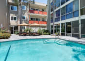 Thumbnail 11 of 47 - Sherman Oaks Apartments - Krystal Terrace - Pool with Umbrella Covered Seating Area, Plants, and View of Apartment Complex