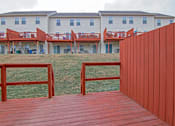 Thumbnail 15 of 48 - A wooden deck with a red fence in front of a white building.