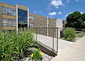 Thumbnail 7 of 12 - A building with a metal fence and plants in front.