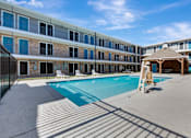 Thumbnail 2 of 8 - A swimming pool is surrounded by sun loungers in front of a building.