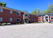Thumbnail 10 of 25 - A large red brick building with a parking lot in front. at Hallwood Manor Apartments, Mentor, 44060