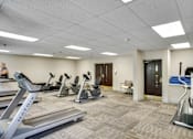 Thumbnail 15 of 30 - A gym with treadmills, elliptical machines, and a woman walking at Independence Place Apartments, Ohio 44130