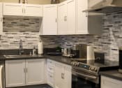 Thumbnail 23 of 75 - a kitchen with white cabinets and black countertops at The Crossings at Redlands, Redlands, CA