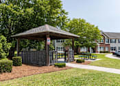 Thumbnail 10 of 10 - A gazebo is surrounded by bushes and a fence at Carriage Hills, Lumberton, NC 28358