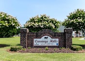 Thumbnail 1 of 10 - A sign for Carriage Hills Apartments is surrounded by bushes and trees at Carriage Hills, 28358