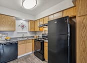 Thumbnail 22 of 24 - A black refrigerator stands in a kitchen with wooden cabinets.