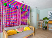 Thumbnail 23 of 34 - A room with a couch and a wall hanging with fruit pillows.