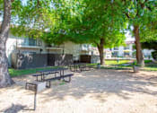 Thumbnail 29 of 34 - A picnic table is in the middle of a sandy area with trees and a building in the background.
