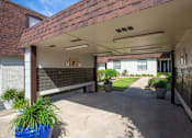 Thumbnail 24 of 34 - A covered walkway leads to a white building with a brick wall and a black fence.
