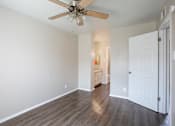 Thumbnail 19 of 34 - A room with a ceiling fan and wooden floors.