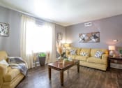 Thumbnail 4 of 34 - A living room with a tan couch, a coffee table, and a lamp.