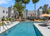 Thumbnail 23 of 42 - A swimming pool surrounded by chairs and trees in front of a building.