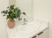 Thumbnail 8 of 12 - A bathroom sink with a pink vase and a mirror above it.