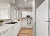 Thumbnail 4 of 23 - A white kitchen with a sink, stove, and refrigerator.