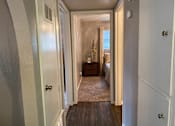 Thumbnail 8 of 13 - A hallway with a door on the left and a bedroom at the end.