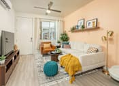 Thumbnail 11 of 12 - A living room with a white couch, a yellow throw blanket, and a blue pouf.