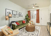 Thumbnail 1 of 12 - A living room with a green couch, a wicker table, and a fan on the ceiling.