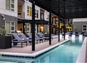 Thumbnail 6 of 28 - A pool area with lounge chairs and a building in the background.