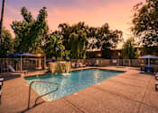 Thumbnail 1 of 17 - A pool surrounded by trees and chairs with a sunset in the background.