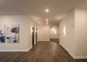 Thumbnail 5 of 23 - a hallway with white walls and wood floors and a painting on the wall