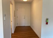Thumbnail 7 of 10 - A hallway with a door and a fire extinguisher on the wall.