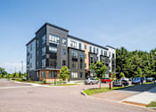 Thumbnail 1 of 30 - A modern multi-story apartment building with cars parked in front.
