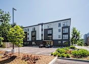 Thumbnail 3 of 30 - A modern building with a parking lot in front.