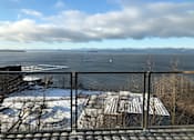 Thumbnail 13 of 18 - A view from a balcony overlooking a snowy landscape with a body of water and mountains in the distance.