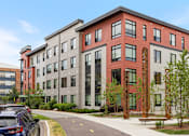 Thumbnail 41 of 44 - A modern building with a red brick facade and a parking lot in front.