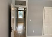 Thumbnail 15 of 24 - A hallway with a white door on the right and a window in the distance.