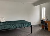Thumbnail 6 of 15 - a bedroom with a bed and a desk with a chair